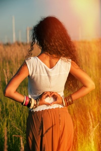young woman back shot in summer field with hands heart sign shape
