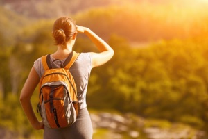 Young backpacker traveling along green mountains on sunrise, happy female walking discovering world, summer vacation concept
